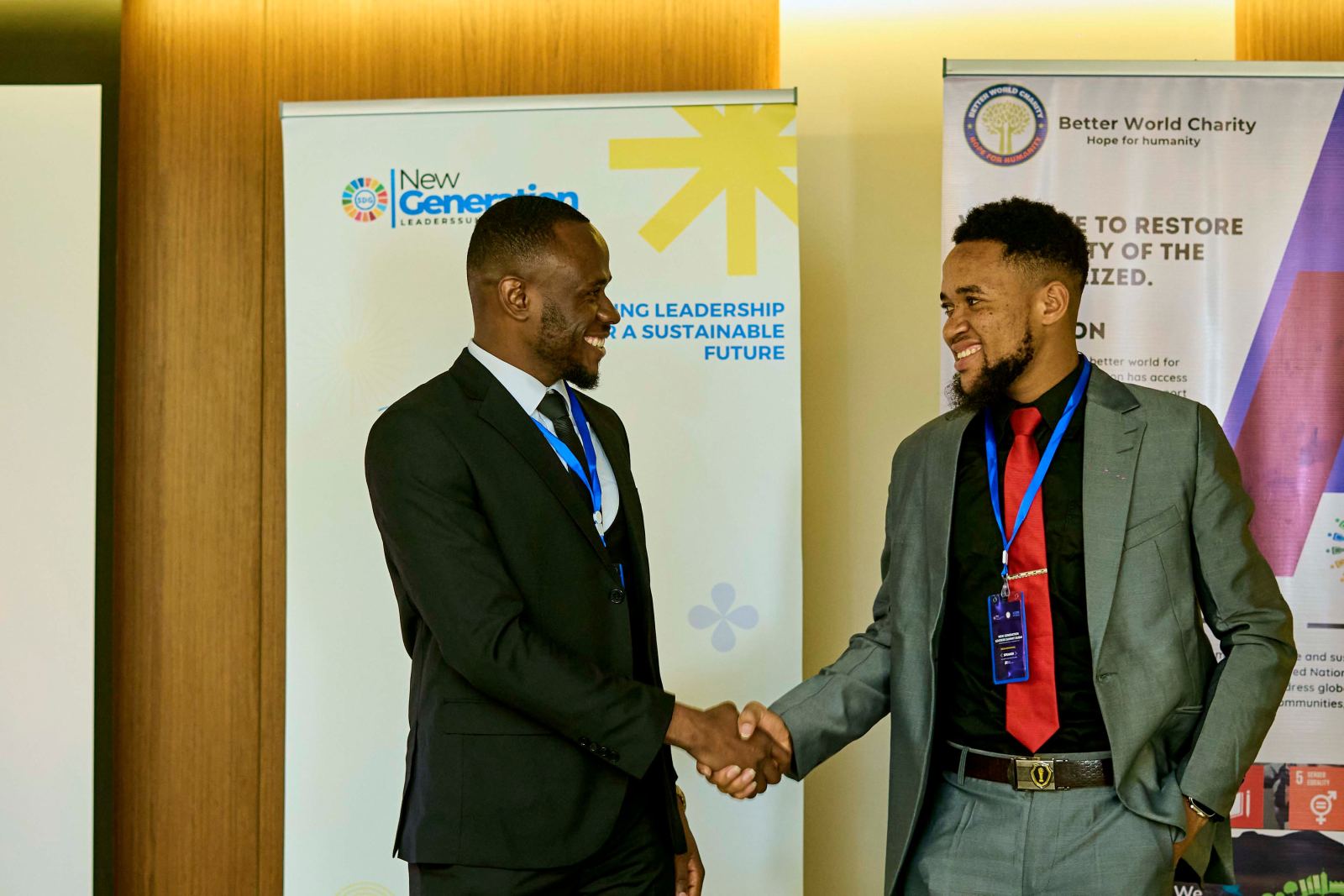 Two men in suits shaking hands between the New Generation and Better World Charity banners
